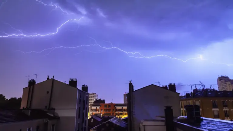 Éclair frappant au-dessus d'immeubles résidentiels lors d'un violent orage nocturne.