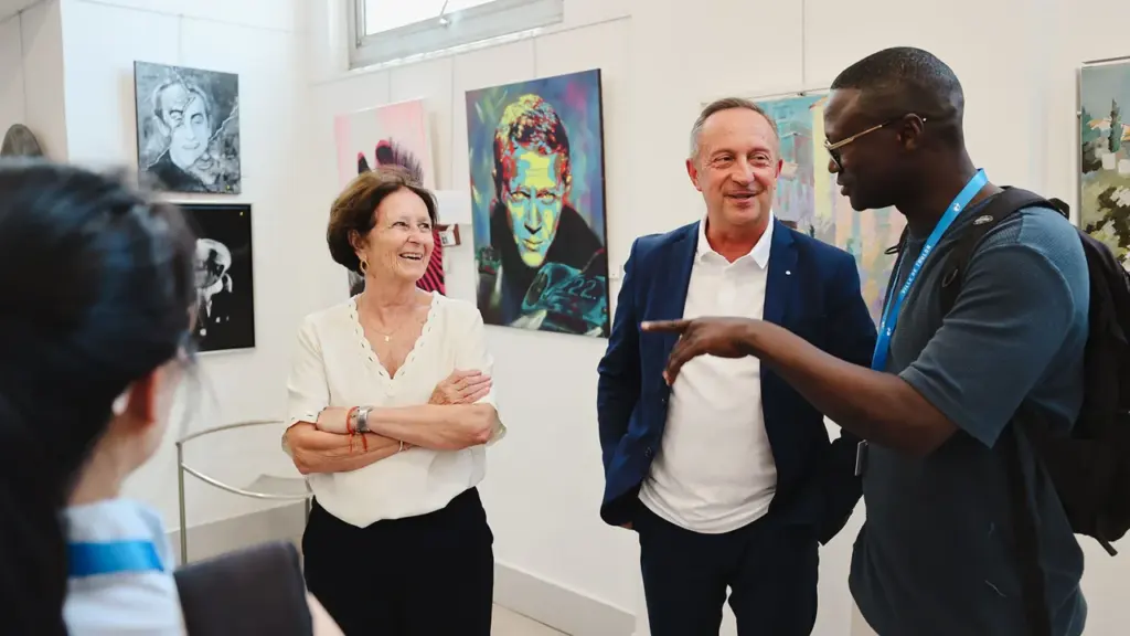 Trois personnes discutent devant des peintures colorées dans une galerie d'art moderne lumineuse.