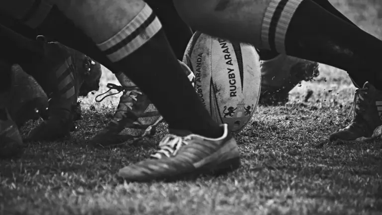 Gros plan en noir et blanc sur un ballon de rugby au sol.