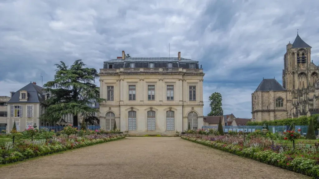 Une élégante bâtisse classique entourée de jardins fleuris avec une cathédrale en arrière-plan.