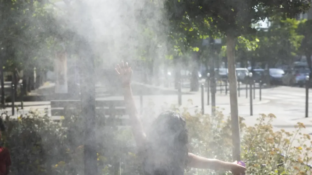 Une personne vue de dos lève les bras dans un nuage de brumisateur urbain.