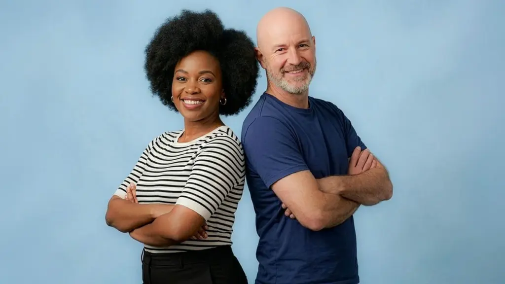 Une femme noire et un homme blanc souriants, posant bras croisés sur fond bleu.