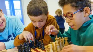 Trois jeunes garçons concentrés jouent aux échecs ensemble autour d'un échiquier dans une salle.