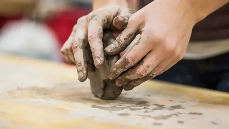 Gros plan sur les mains d'un participant travaillant l'argile lors d'un atelier de modelage.