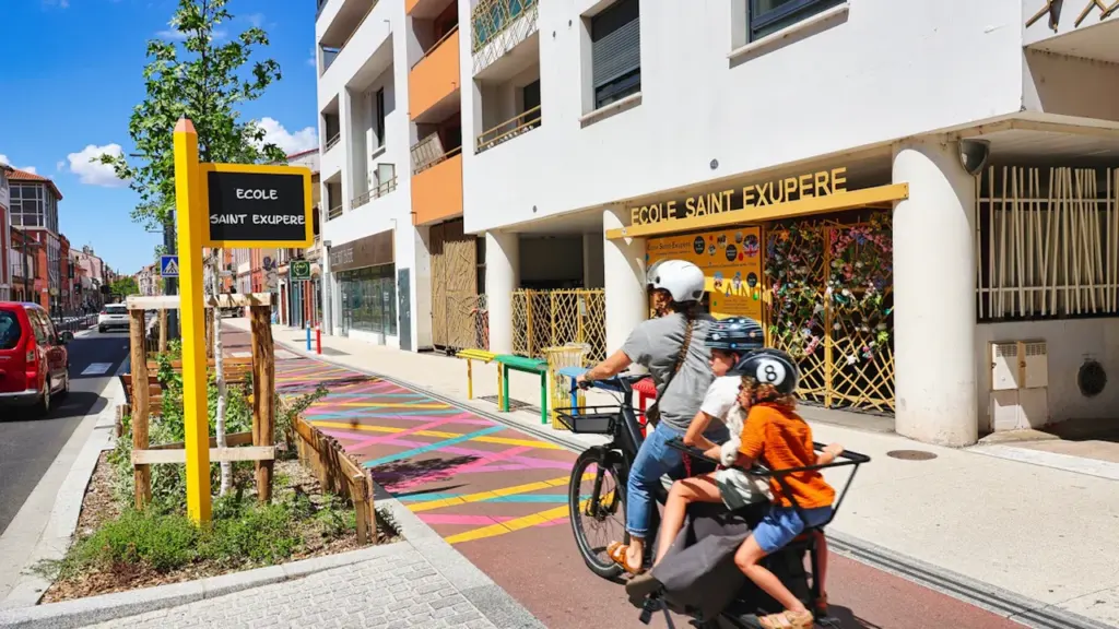 Famille à vélo devant une école primaire moderne avec des aménagements urbains sécurisés.