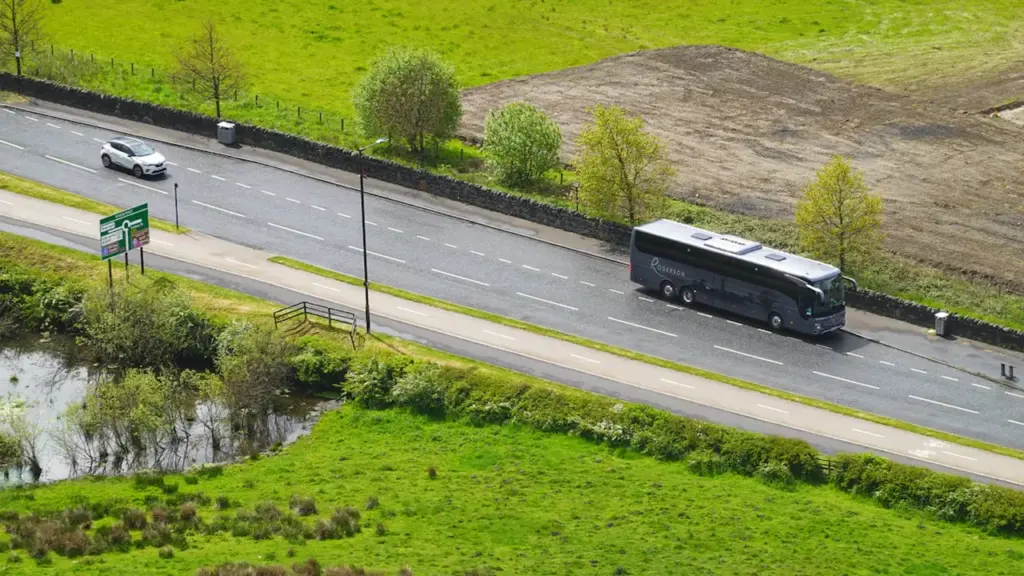 Un autocar de tourisme moderne circulant sur une route de campagne ensoleillée.