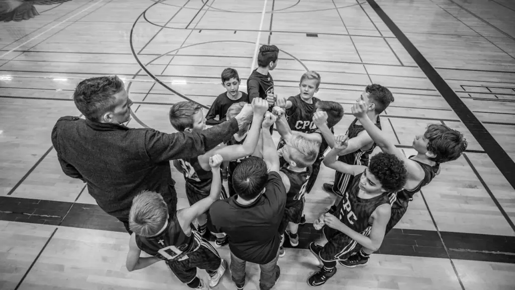 Une équipe de sport en cercle, main dans la main, sur un terrain intérieur.